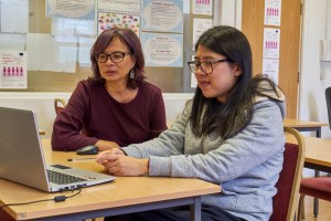 Two adults of different generations sitting in front of a laptop in a classroom type setting.